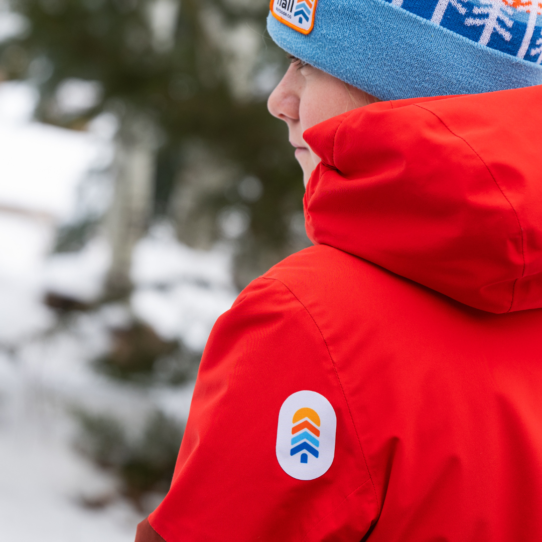 Child wearing a red jacket with a snowy gray NOSO Gear Repair Patch on the shoulder, perfect for fixing tears from outdoor play while adding Town Hall style.